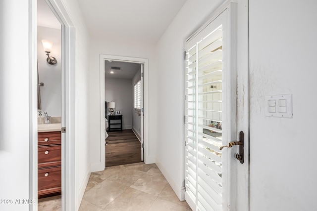 hallway with a sink, visible vents, baseboards, and light tile patterned flooring