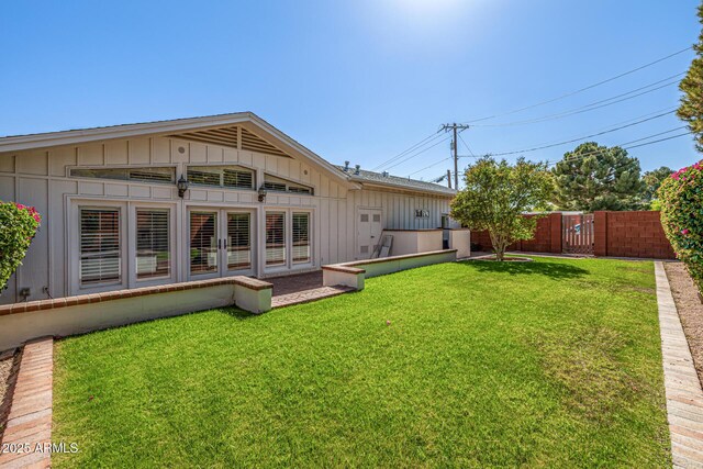 back of property with french doors, board and batten siding, fence, and a lawn