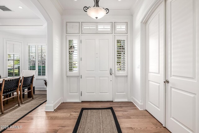 entryway featuring light wood-style floors, arched walkways, ornamental molding, visible vents, and baseboards