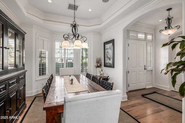 dining space with a notable chandelier, visible vents, a raised ceiling, arched walkways, and wood finished floors