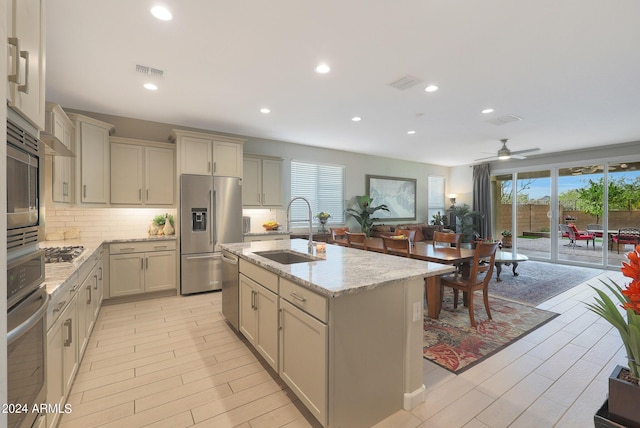 kitchen with visible vents, appliances with stainless steel finishes, a sink, light stone countertops, and backsplash