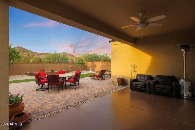 patio terrace at dusk with a ceiling fan, outdoor dining area, a fenced backyard, and a mountain view