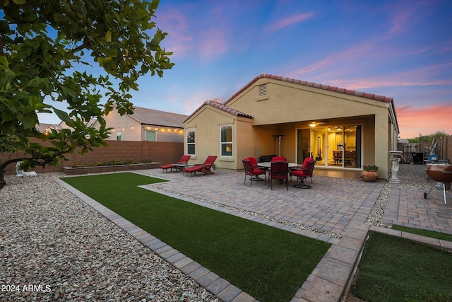 back of house at dusk with a tiled roof, a patio, fence private yard, and stucco siding