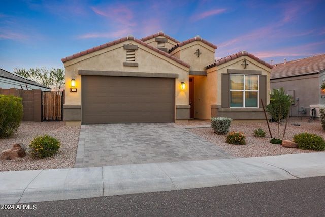 mediterranean / spanish-style house featuring a garage, a tiled roof, fence, decorative driveway, and stucco siding