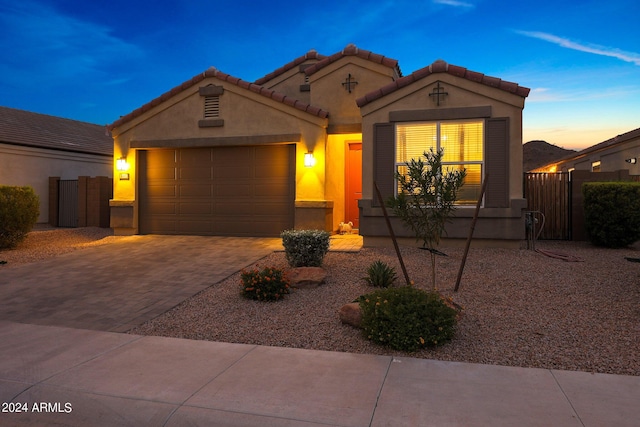 mediterranean / spanish-style house featuring an attached garage, fence, a tiled roof, decorative driveway, and stucco siding