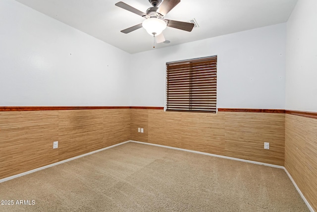 empty room featuring carpet floors, ceiling fan, and wood walls