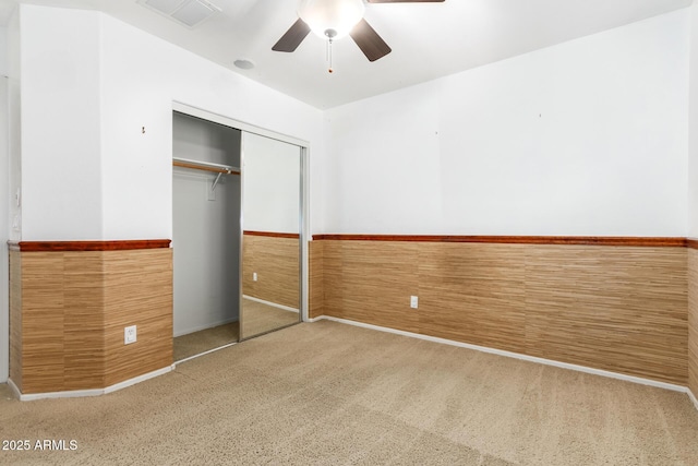 unfurnished bedroom featuring carpet flooring, ceiling fan, a closet, and wood walls