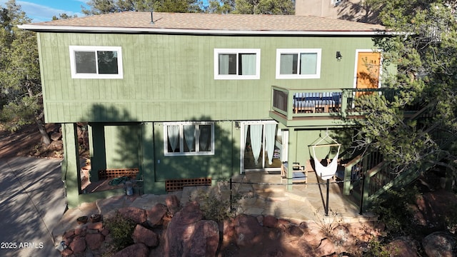 back of property with roof with shingles and a patio