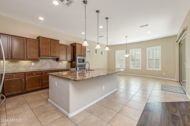 kitchen with backsplash, stainless steel appliances, decorative light fixtures, a center island with sink, and stone counters