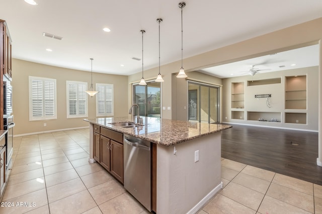 kitchen with light wood-type flooring, stainless steel appliances, sink, decorative light fixtures, and an island with sink