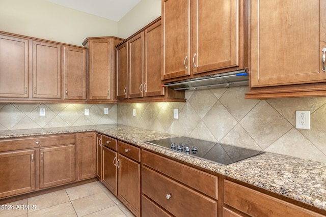 kitchen with tasteful backsplash, light stone countertops, black electric stovetop, and light tile patterned floors