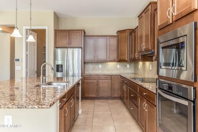 kitchen featuring pendant lighting, a kitchen island with sink, sink, appliances with stainless steel finishes, and tasteful backsplash