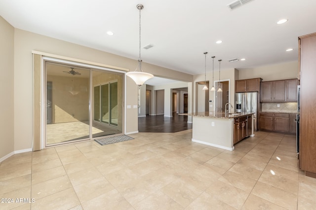 kitchen with tasteful backsplash, light stone counters, sink, pendant lighting, and a center island with sink