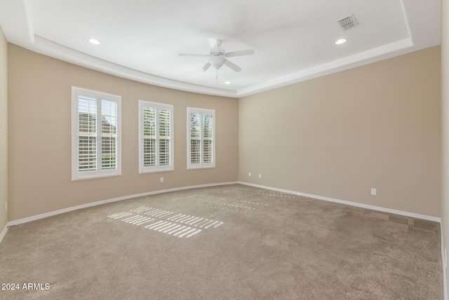 spare room featuring a tray ceiling, light carpet, and ceiling fan