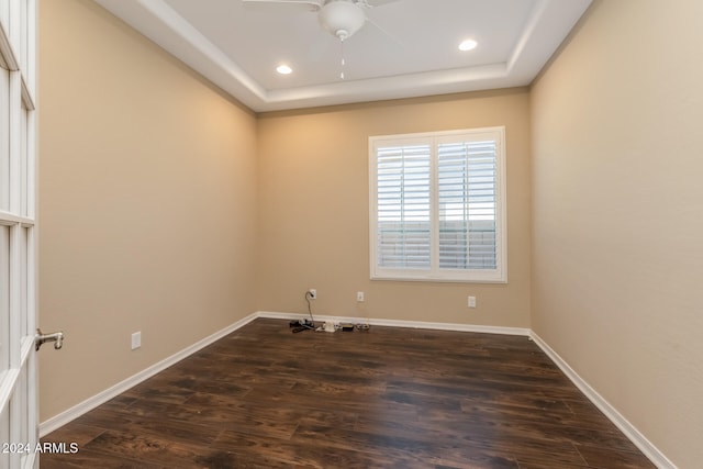 unfurnished room featuring a raised ceiling, ceiling fan, and dark wood-type flooring