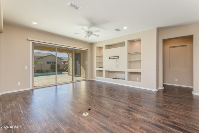 unfurnished living room with built in shelves, ceiling fan, and dark wood-type flooring