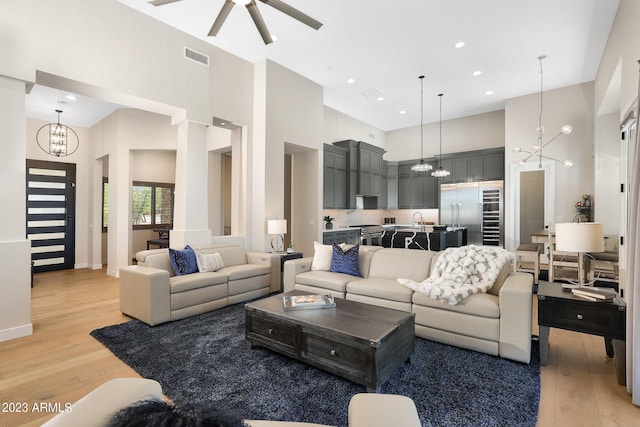 living room with visible vents, a towering ceiling, light wood finished floors, and ceiling fan with notable chandelier