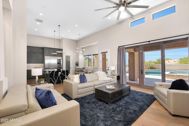 living room with visible vents, a towering ceiling, ceiling fan with notable chandelier, light wood-type flooring, and recessed lighting