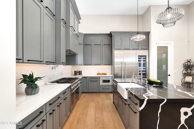 kitchen with decorative backsplash, high end appliances, light wood-style flooring, gray cabinetry, and a sink