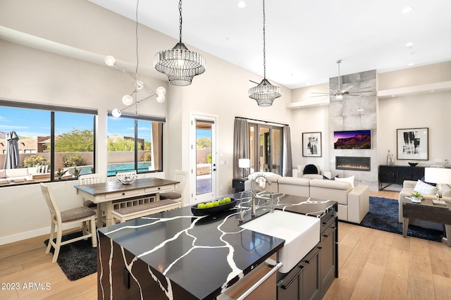 kitchen with light wood-type flooring, pendant lighting, a high ceiling, and a tiled fireplace