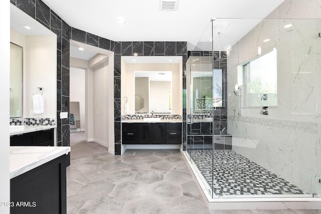 full bath featuring a sink, two vanities, visible vents, tile walls, and a shower stall