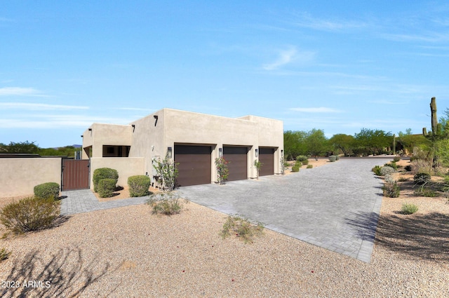 pueblo-style home with decorative driveway, an attached garage, a gate, and stucco siding