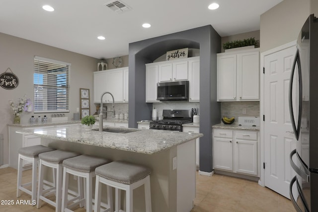 kitchen featuring a breakfast bar area, stainless steel appliances, a sink, visible vents, and white cabinets