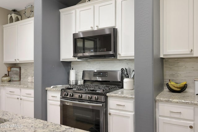 kitchen featuring stainless steel appliances, white cabinetry, decorative backsplash, and light stone countertops