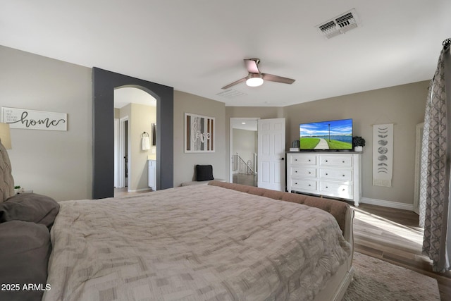 bedroom featuring baseboards, visible vents, arched walkways, ceiling fan, and wood finished floors