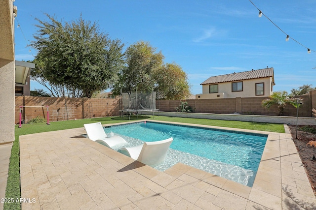 view of swimming pool featuring a patio, a yard, a trampoline, and a fenced backyard