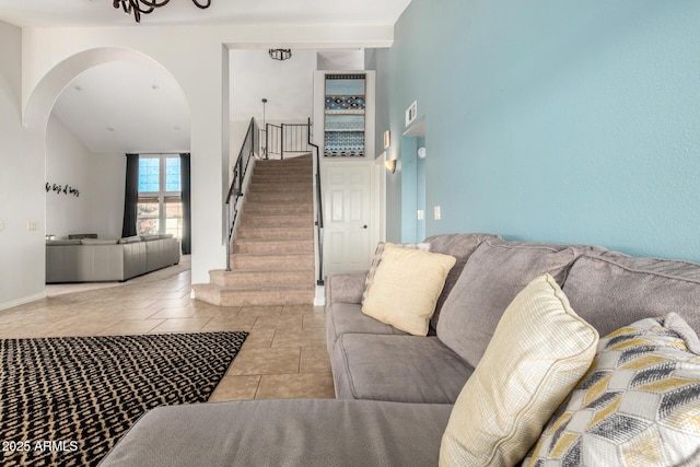 tiled living room with arched walkways, stairs, a towering ceiling, and baseboards