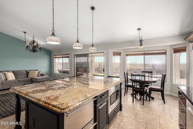 kitchen featuring stainless steel microwave, vaulted ceiling, pendant lighting, light stone counters, and a kitchen island