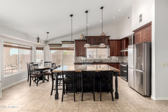 kitchen with appliances with stainless steel finishes, vaulted ceiling, decorative backsplash, a center island, and a sink