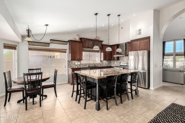 kitchen featuring appliances with stainless steel finishes, vaulted ceiling, a sink, wall chimney exhaust hood, and backsplash