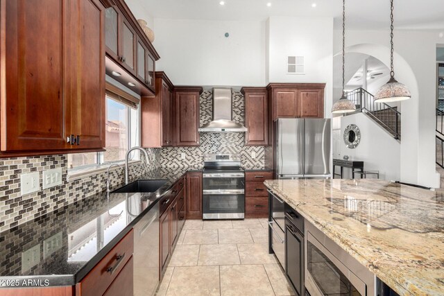 kitchen with wall chimney exhaust hood, appliances with stainless steel finishes, a sink, dark stone counters, and recessed lighting