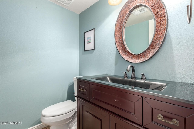 bathroom featuring toilet, vanity, and a textured wall