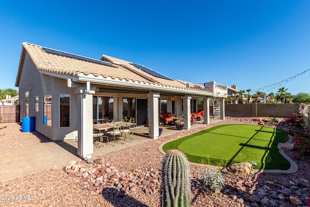 rear view of house featuring an area to practice putting, a fenced backyard, a patio area, a tiled roof, and solar panels