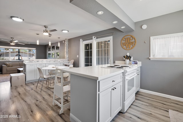 kitchen with a peninsula, a ceiling fan, white electric stove, open floor plan, and a breakfast bar area
