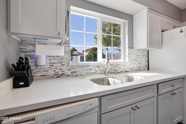 kitchen with a sink, light countertops, tasteful backsplash, and white dishwasher