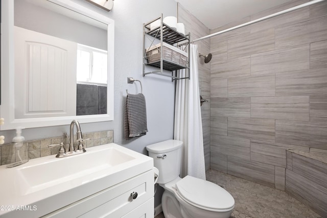 bathroom with toilet, tiled shower, and vanity