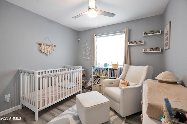 bedroom with a nursery area, baseboards, a ceiling fan, and wood finished floors