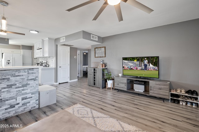 living room featuring light wood finished floors, visible vents, and a ceiling fan