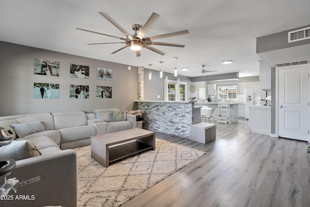 living room with visible vents, light wood-type flooring, and a ceiling fan