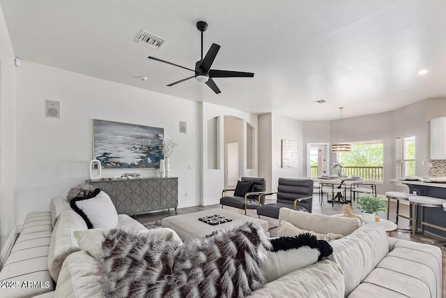 living room featuring baseboards, arched walkways, ceiling fan, visible vents, and wood finished floors