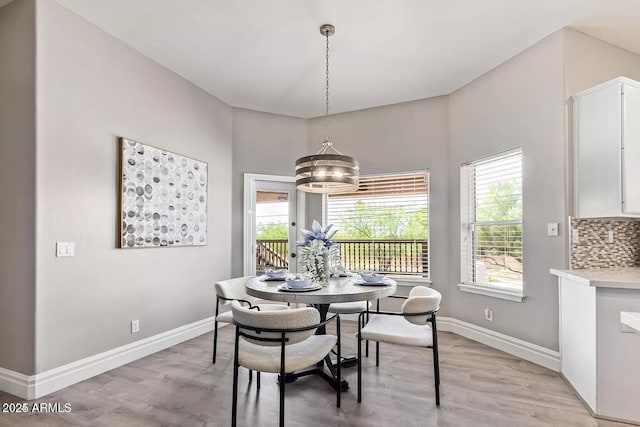 dining space with light wood-style flooring, a notable chandelier, and baseboards
