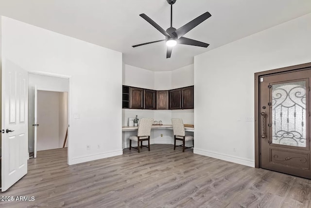 interior space featuring baseboards, built in study area, a ceiling fan, and light wood-type flooring