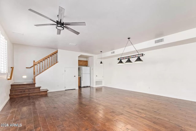 unfurnished living room featuring dark wood-type flooring, stairs, ceiling fan, and visible vents