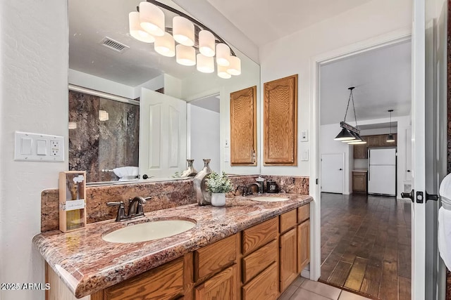 full bathroom featuring a shower with door, visible vents, a sink, and double vanity