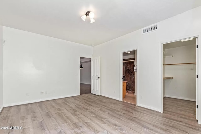 unfurnished bedroom featuring a spacious closet, wood finished floors, a closet, and visible vents