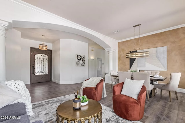 living area with decorative columns, wood finished floors, baseboards, arched walkways, and ornamental molding